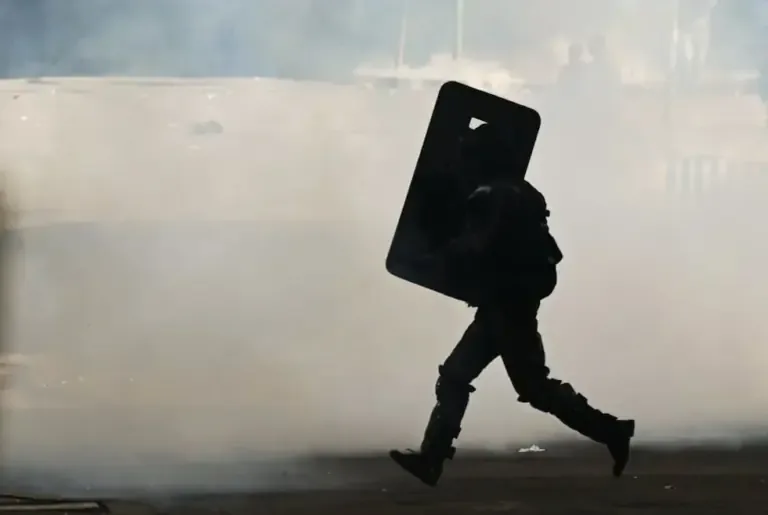 A riot police officer uses his shield during clashes at a demonstration against President Rodrigo Paz in La Paz, Bolivia, on May 25, 2026. (Photo by Marvin RECINOS / AFP).