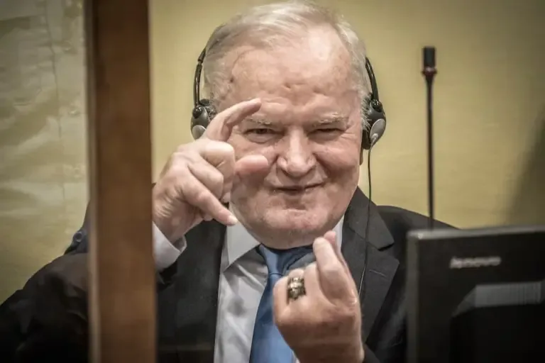 Ratko Mladic pretends to take photographs while sitting in the dock before the final appeal verdict hearing against his genocide conviction for the Srebrenica massacre. (Photo by Jerry Lampen / ANP / AFP).