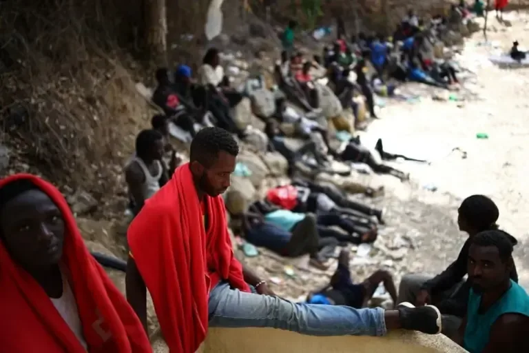 Several migrants remain seated in front of the temporary reception center CETI in Ceuta, Spanish enclave in North Africa, on August 1, 2026. (Henry Nicholls / AFP)